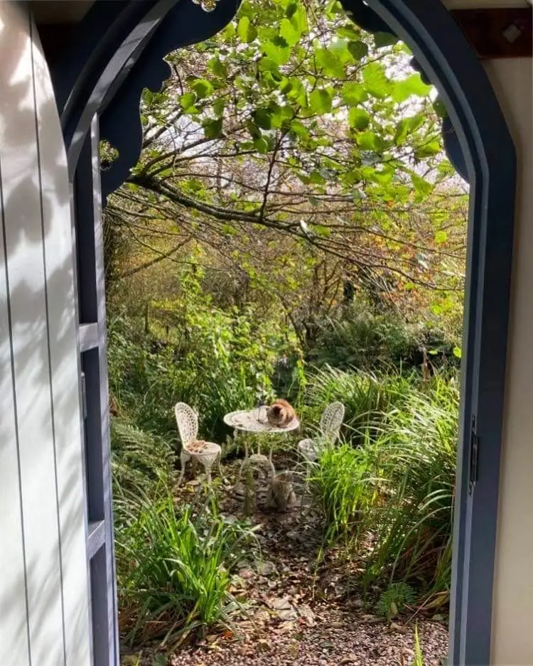 View through the arched door to a little garden table and chairs, with a cat