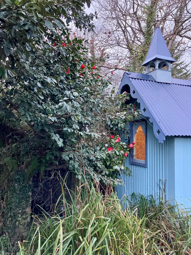 Stained glass window and the hut's little spire beside a red camellia