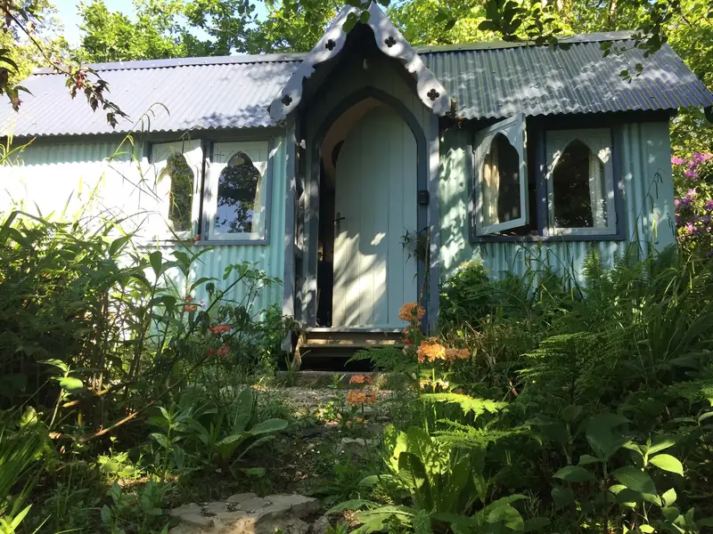 The front of The Tabernacle, a pale blue gothic shepherd's hut, framed by ferns and flowers